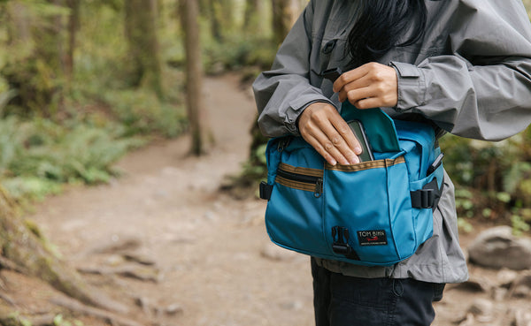 Person accessing a phone from the front buckle pocket of the LGD while wearing it as a waist pack.